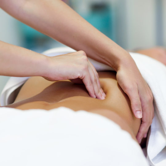 Female patient is receiving treatment by professional osteopathy therapist. Woman having abdomen massage in a physiotherapy center.